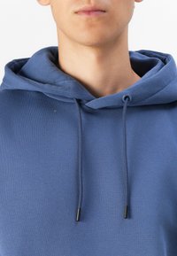 Sudadera azul con capucha ajustable, con puntas metálicas negras en los cordones y una tela suave, ligeramente texturizada.