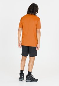 Kortärmad orange sporttröja, tillsammans med svarta shorts och svarta vandringsskor. Slät textur med en avslappnad passform, inga synliga logotyper.