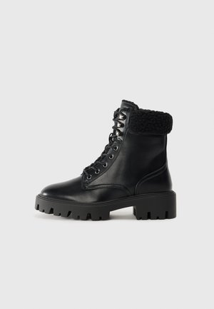 Mustad mustad musta nahast lace-up pahkluu saapad tekstuuriga mustast kunstkarusnahast äärisega, korraliku kanna ja robustse kummist talla, millel on sügavad sooned.