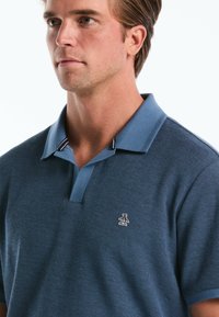 Polo bleu en tissu texturé, avec un col contrasté et un petit logo brodé sur la poitrine gauche. Manches courtes, coupe classique.