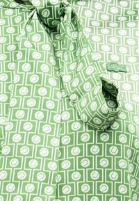 Chemise verte avec un motif géométrique blanc de balles de tennis et une écharpe nouée assortie drapée sur le col.
