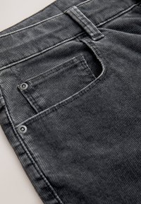 Tissu en velours côtelé noir avec une poche arrière munie de deux rivets en métal, présentant une texture verticale et un bord fini propre.