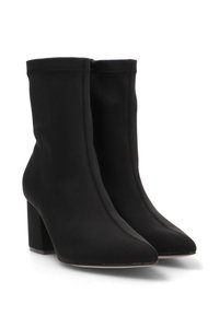 Botas de tobillo negras con un upper de tejido liso y elástico, punta afilada y tacón cuadrado. Cuenta con costuras mínimas y un diseño elegante.