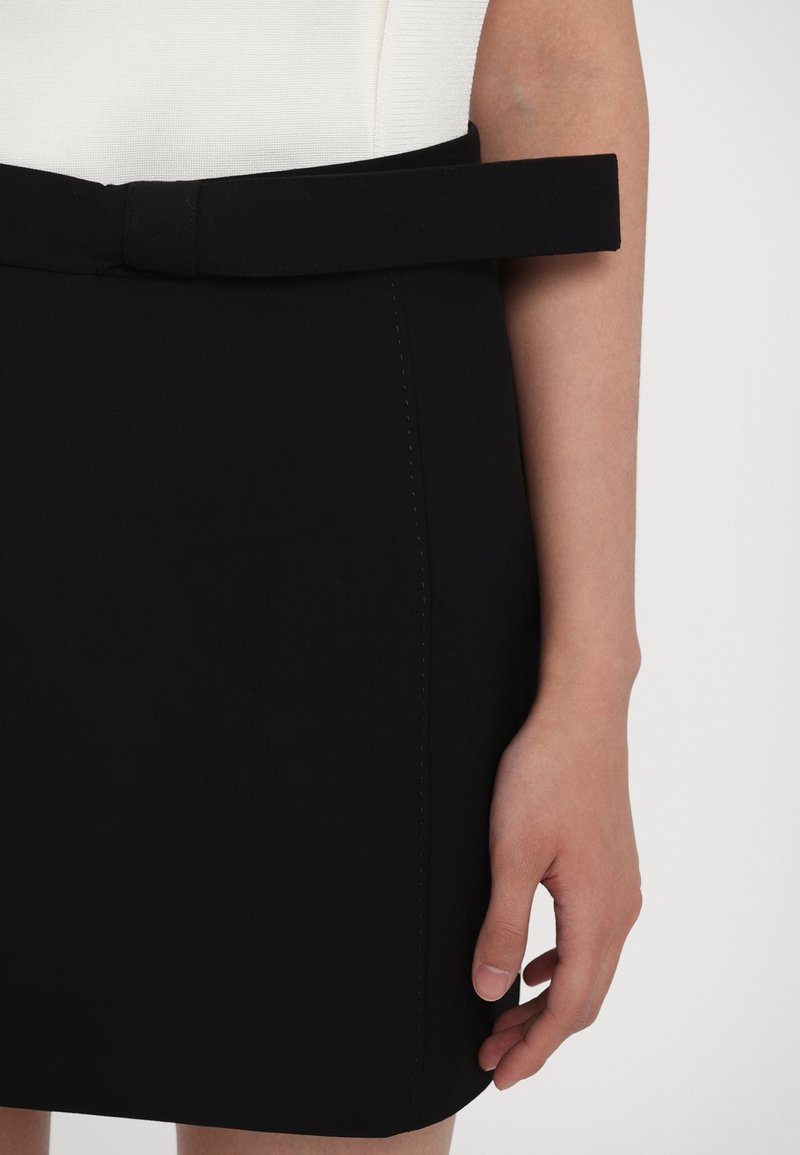 Black skirt with a smooth texture, featuring a wide waistband and a fabric belt. The hem is straight, with minimal stitching detail.