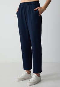 Marineblauwe elastische broek met zijzakken, met een rechte snit en zichtbare stiknaaddetails, gecombineerd met witte sneakers.