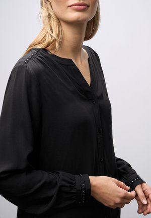 Černá dlouhá blůza s volným střihem, zapínání na knoflíky vpředu, s výstřihem do V a dekorativními cvočky na ramenou a manžetách. Měkká textilie.