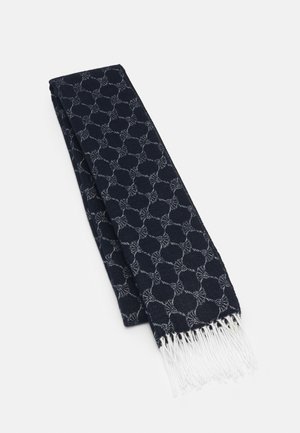 Écharpe bleu marine pliée, présentant un motif circulaire gris clair et des extrémités blanches à franges, posée sur une surface blanche.