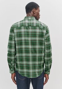 Green plaid shirt with long sleeves, featuring a button-down collar, white and dark green lines, and a curved hem at the back.