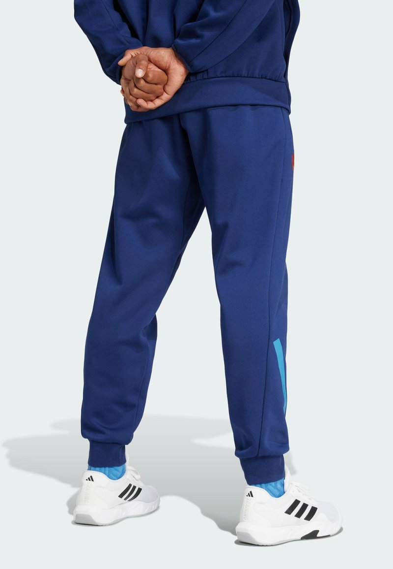 Marineblaue Jogginghose mit schmalem Schnitt, die an der Seite einen blauen Akzent hat und mit elastischen Bündchen abschließt, kombiniert mit weißen Sportschuhen.
