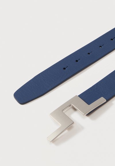 Μπλε δερμάτινη ζώνη με αγκράφα ασημί σε σχήμα ζιγκ ζαγκ και πολλαπλές τρύπες για ρύθμιση, σε λευκό φόντο.