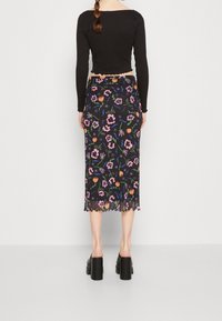 Svart långärmad topp med scallopkant, parat med en blommönstrad midiklänning i svart med rosa och orange blommor. Svarta platåskor.