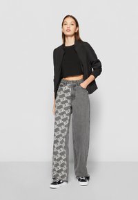 Svart cropped bomberjakke, tettsittende svart topp, grå denimbukser med mønstret side, og sorte joggesko. Uformelt antrekk med distinkte teksturer.