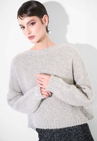 Maglione di colore grigio chiaro, lavorato a maglia grossa, con vestibilità ampia, ampia scollatura e maniche lunghe. Presenta una superficie leggermente strutturata e un orlo a coste.
