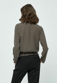 Blusa a maniche lunghe nera e beige con motivo, scollo rotondo e orlo arricciato. Indossata con pantaloni neri.