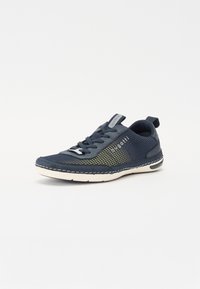 Zapatilla deportiva de color navy con parte superior de malla, acentos amarillos y una suela blanca. Superficie texturizada con ribete cosido y una lengüeta en el talón.