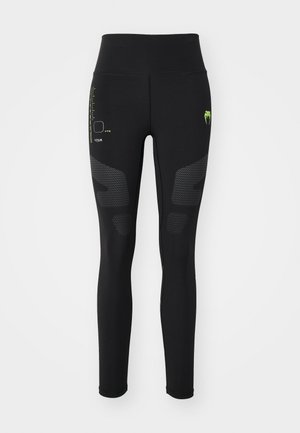 Black athletic leggings with a high waistband, featuring textured panel accents and green logo details, designed for performance and comfort.