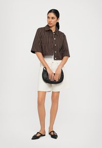 Brown striped cropped button-up shirt, white high-waisted shorts, black woven handbag, and black flat shoes. Smooth textures and tailored fit.
