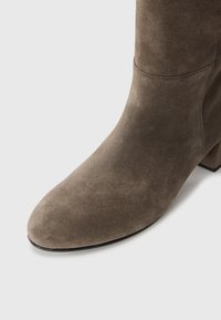 Bottine en cuir suédé marron discret avec un bout arrondi, une surface texturée et un talon carré, présentant des coutures minimales pour un design épuré.