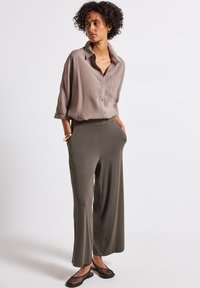 Chemise beige à manches longues avec des boutons et une poche poitrine ; pantalon large olive avec des poches latérales ; ballerines en mesh noires.