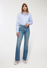 Jasnoniebieska w paski koszula z guzikami, spodnie dzwony z wysokim stanem w jasnym odcieniu, oraz białe buty na szpic. Gładkie faktury i klasyczny design.