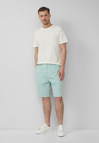 Hellgraues T-Shirt, kurze Ärmel. Mintgrüne Shorts mit Kordelzug, zwei seitlichen Taschen. Weiße Sneaker mit strukturierter Oberfläche, runde Spitze.