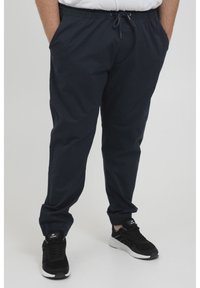Marineblauwe elastische broek met een trekkoord, zijzakken en taps toelopende broekspijpen. G gedragen met zwarte sportsneakers.