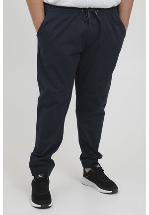 Navy blue elastic-waist pants with a drawstring, side pockets, and tapered leg cuffs. Worn with black athletic sneakers.