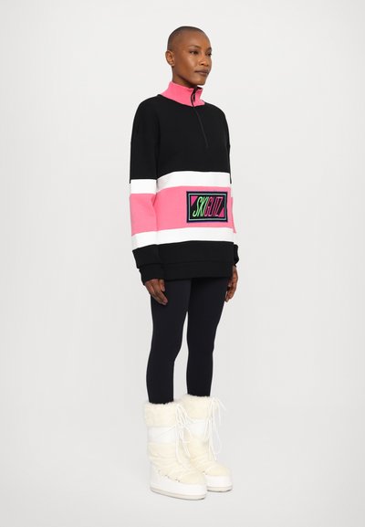 Hanorac cu fermoar negru și roz, cu dungi albe, având un patch cu logo, asortat cu colanți negri și cizme cu blană albă.