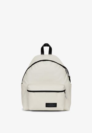 Rucksack aus cremefarbenem Stoff mit abgerundeter Form, ausgestattet mit einer vorderen Reißverschlusstasche und schwarzen Akzenten an den Rändern und dem Logo.