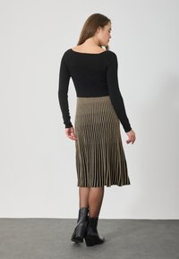Melna garām piedurknēm pieguļošā blūze apvienota ar ceļa garuma svārkiem ar vertikālām zelta svītrām. Modelis valkā melnus potīšu zābakus. Minimalistisks fons.