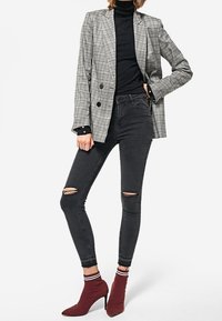 Šedý kostkovaný dvouřadý blejzr přes černý rolák, kombinovaný s černými skinny džíny s roztrhanými koleny a červenými kotníkovými botami.