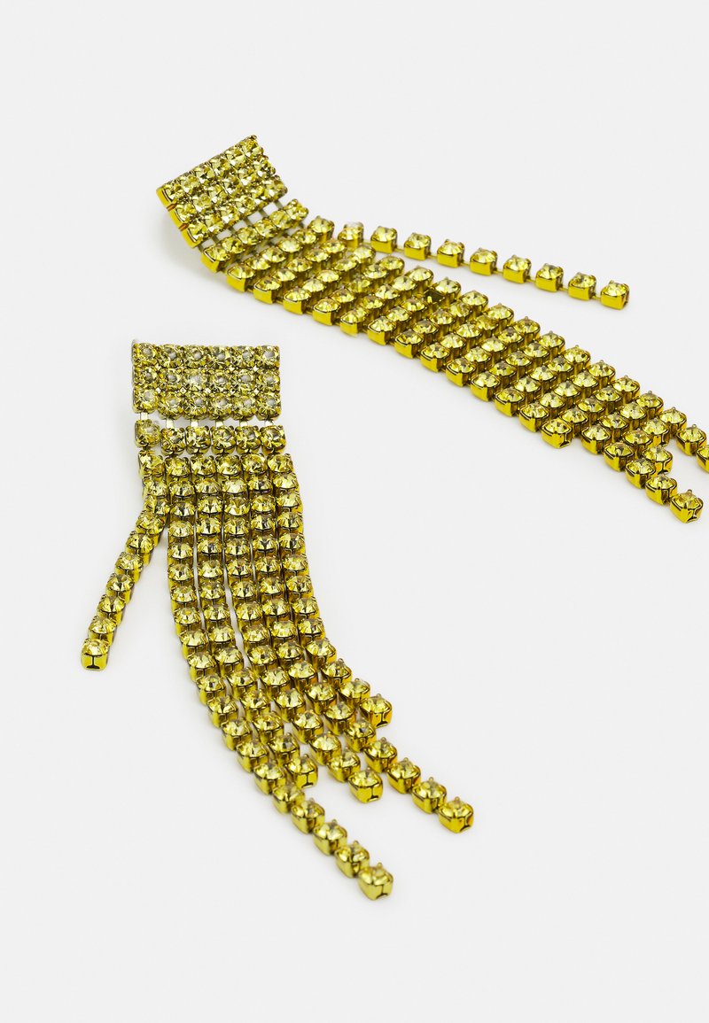 Orecchini a chandelier in tono oro con più file di piccoli cristalli quadrati gialli disposti in un design a frangia su uno sfondo bianco.