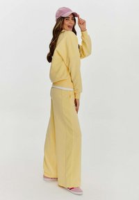 Žlutá bavlněná mikina a široké kalhoty, doplněné růžovou kšiltovkou a teniskami s růžovými akcenty, s hladkou strukturou.