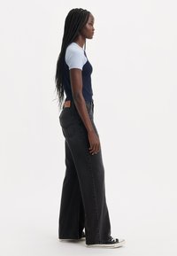 Jean large noir et haut ajusté bicolore en marine et bleu clair. Les jeans présentent un patch logo en cuir sur la ceinture arrière.