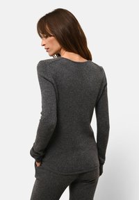 Donkergrijze lange mouwen trui gemaakt van gestructureerde stof. Heeft een ronde hals en is aangesloten bij de taille, met bijpassende grijze onderkleding.