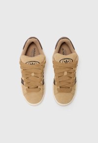 Tan suede sneakers with brown accents, flat laces, rubber soles, and the Adidas logo on the tongue. Smooth texture and rounded toe design.