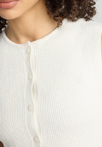 White ribbed knit sleeveless top featuring a round neckline and five translucent buttons along the front. Textured fabric throughout.