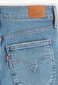 Ljusblå denimjeans med en läderetikett vid midjan, bakficka med bågformad sömnad och en röd etikett på fickan.