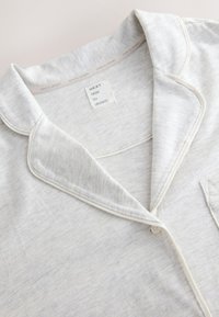 Light gray pajama top made of soft, textured fabric. Features a notched collar, contrasting white piping, and a chest pocket.