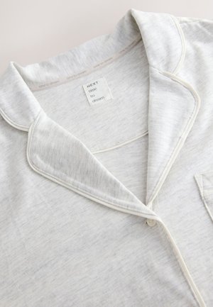 Hellgraues Pyjama-Oberteil aus weichem, strukturiertem Stoff. Verfügt über einen Reverskragen, kontrastierende weiße Paspelierung und eine Brusttasche.