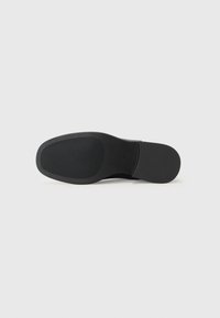 Suela de zapato negra con una superficie lisa y un patrón estriado para mayor agarre. Diseñada para ofrecer estabilidad con una puntera redondeada y una construcción sólida.