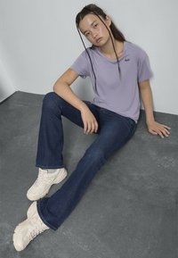 T-shirt lavanda a maniche corte con logo "Levi's", jeans a zampa d'elefante blu scuro e sneaker bianche. Tessuto liscio e vestibilità casual.
