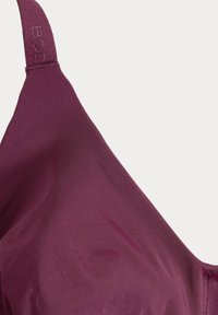 Burgundská podprsenka z hladké látky. Má nastavitelné ramínka, elegantní design a jemný textový detail na ramínku.