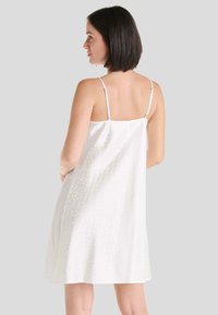 Vestido deslizante de satén blanco con tirantes finos ajustables, que presenta un sutil patrón texturizado. Dobladillo en A fluido, acabado suave.
