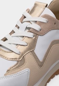 Λευκό αθλητικό παπούτσι με πάνελ σε μπεζ, ταμπά και μεταλλικό χρυσό, υφή δέρματος, λευκά κορδόνια και λαστιχένια σόλα.