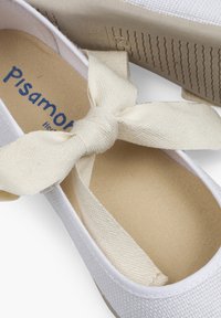Witte canvas espadrilles met een beige stoffen strik aan de voorkant, een textuurzool en een rubberen buitenzool met een golvend patroon.