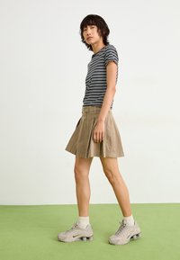 Stripet kortærmet skjorte, beige plisseret nederdel og grå træningssko med luftpolstring. Simple design med en afslappet pasform.