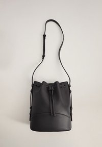 Sac seau en cuir noir avec fermeture à cordon, bandoulière réglable et texture lisse, avec une couture horizontale contrastante à la base.