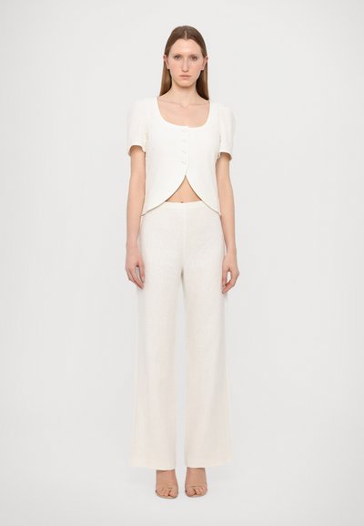 Top blanco recortado con botones y mangas cortas abullonadas, combinado con pantalones anchos blancos. La tela parece ligera y tiene una textura suave.