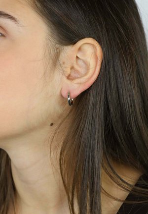 Pendiente de aro plateado exhibido en la oreja, con una superficie lisa y pulida y un diseño circular. El cabello cae suavemente junto a la oreja.